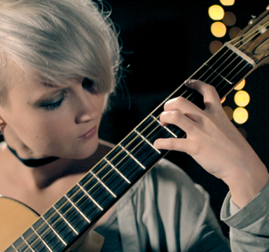 photo of a young person with silver hair playing a chord on a guitar