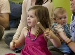 child in pink plays with drum sticks