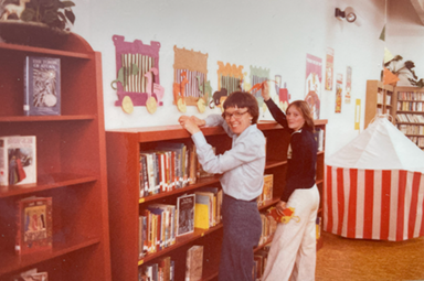 two people standing in front of library shelves in vintage photograph