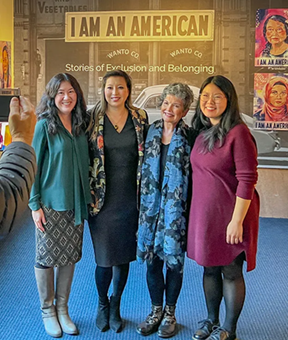 four people posing for photo in front of 'i am an american' sign